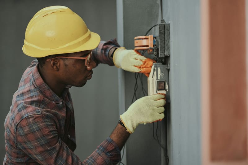 A technician in a hard hat tests wiring at an electrical panel